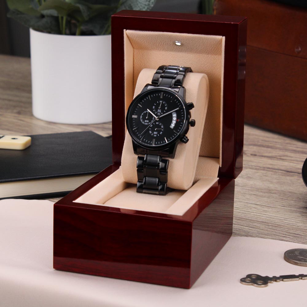 Black wristwatch in a wooden display box on a wooden surface with a plant in the background.