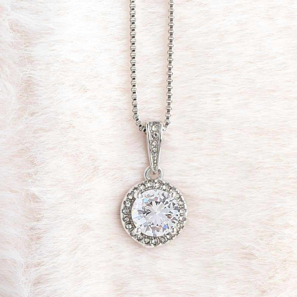 Close-up of a circular cubic zirconia crystal silver pendant necklace resting on white fur texture background.