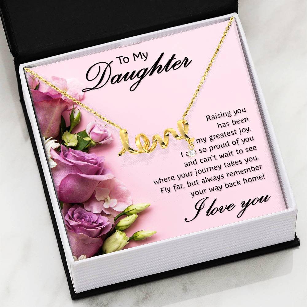 A gold necklace with a cursive 'love' pendant displayed on a pink gift box printed with floral graphics and a sentimental message for a daughter in a black and white gift box with a white marble background.