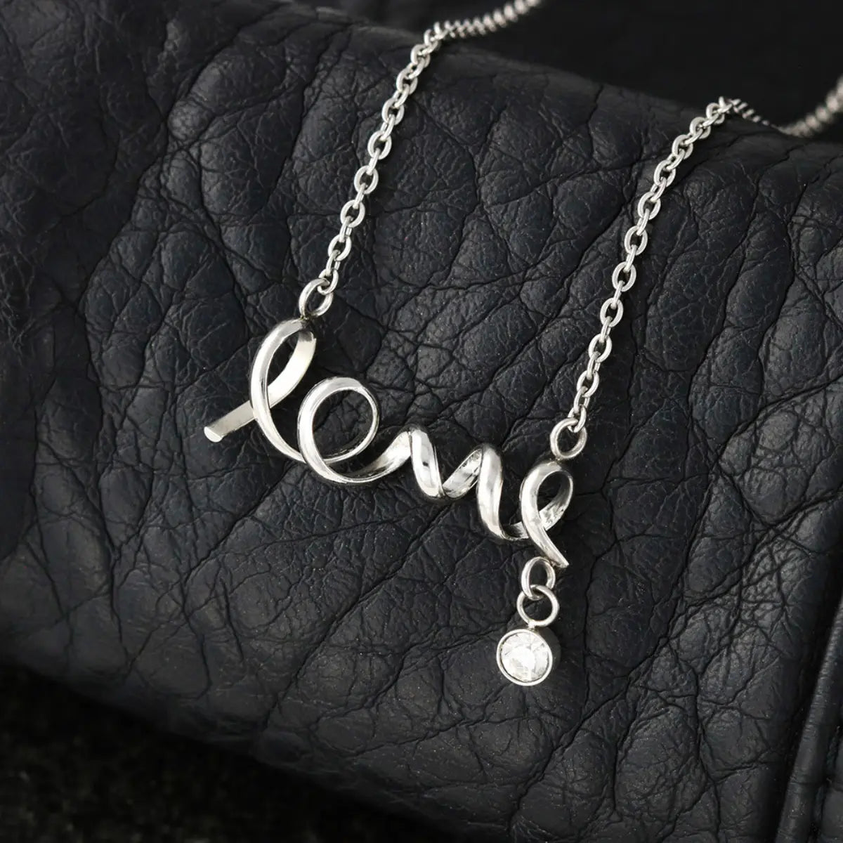 Silver necklace with 'love' pendant on a textured black surface