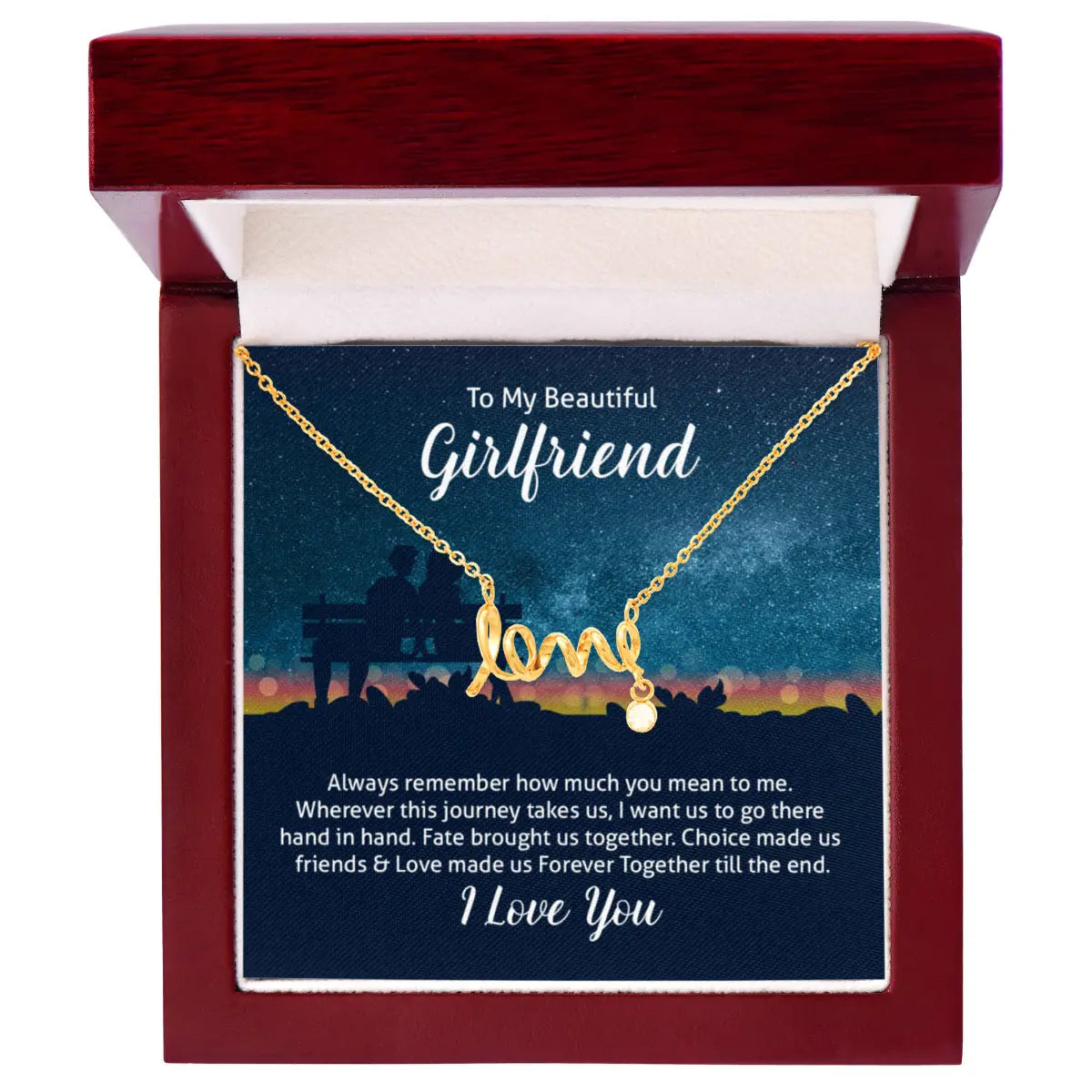 A gold necklace with a 'love' word charm and a small heart pendant, presented inside a dark red wooden gift box. The necklace is displayed on a printed card that reads 'To My Beautiful Girlfriend' and includes a romantic message at the bottom.