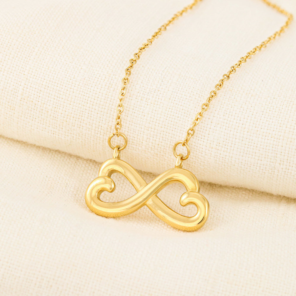 A gold infinity heart pendant necklace presented on a white gift box with a printed birthday message for a wife.