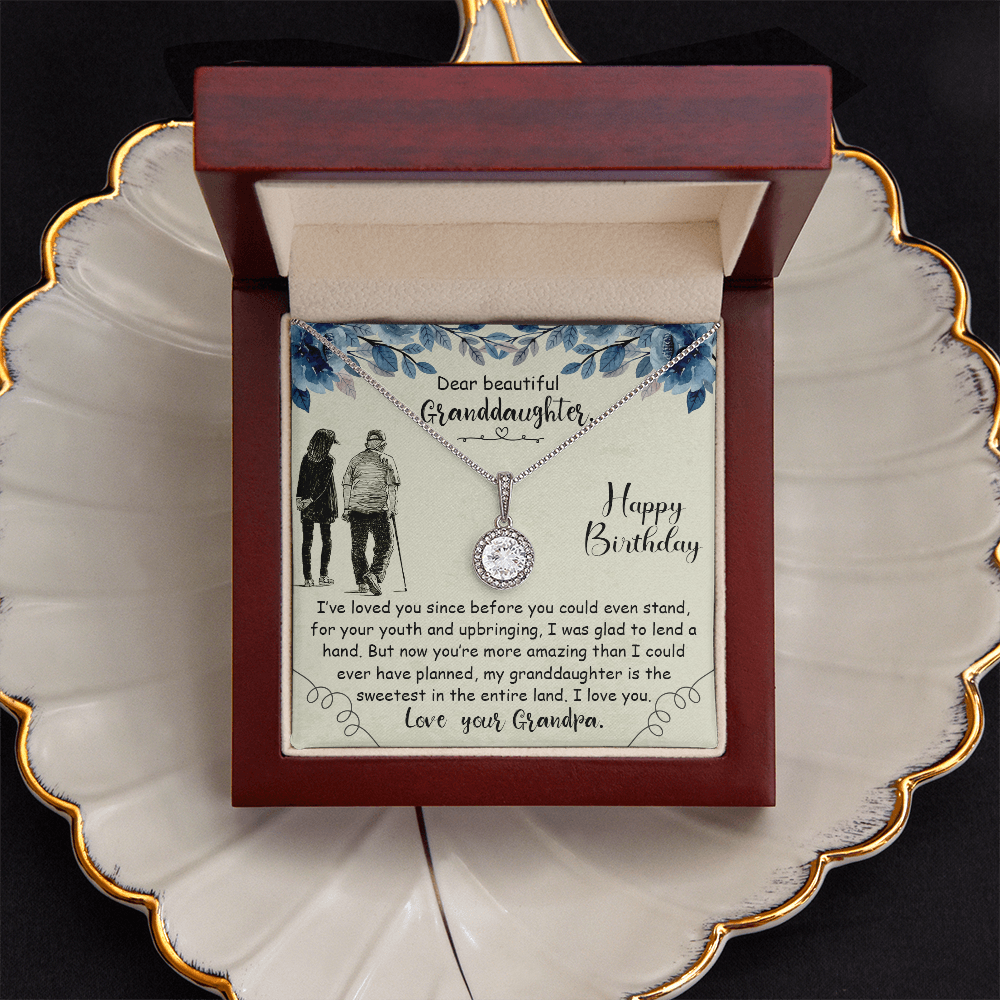 Silver round gemstone necklace on a birthday card inside an illuminated mahogany LED box, sitting on a gold-rimmed ceramic leaf jewelry plate.