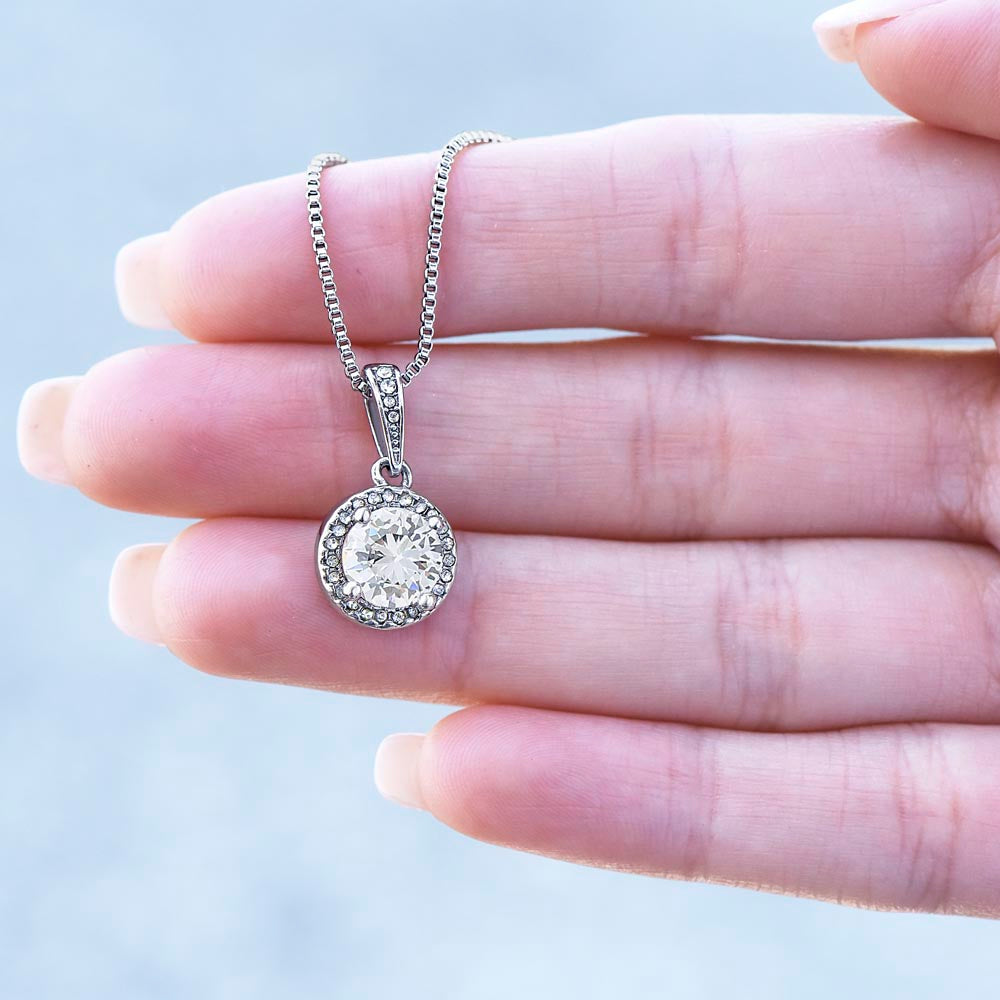 Open palm holding a silver pendant necklace with a brilliant circular cubic zirconia gemstone to show its scale.