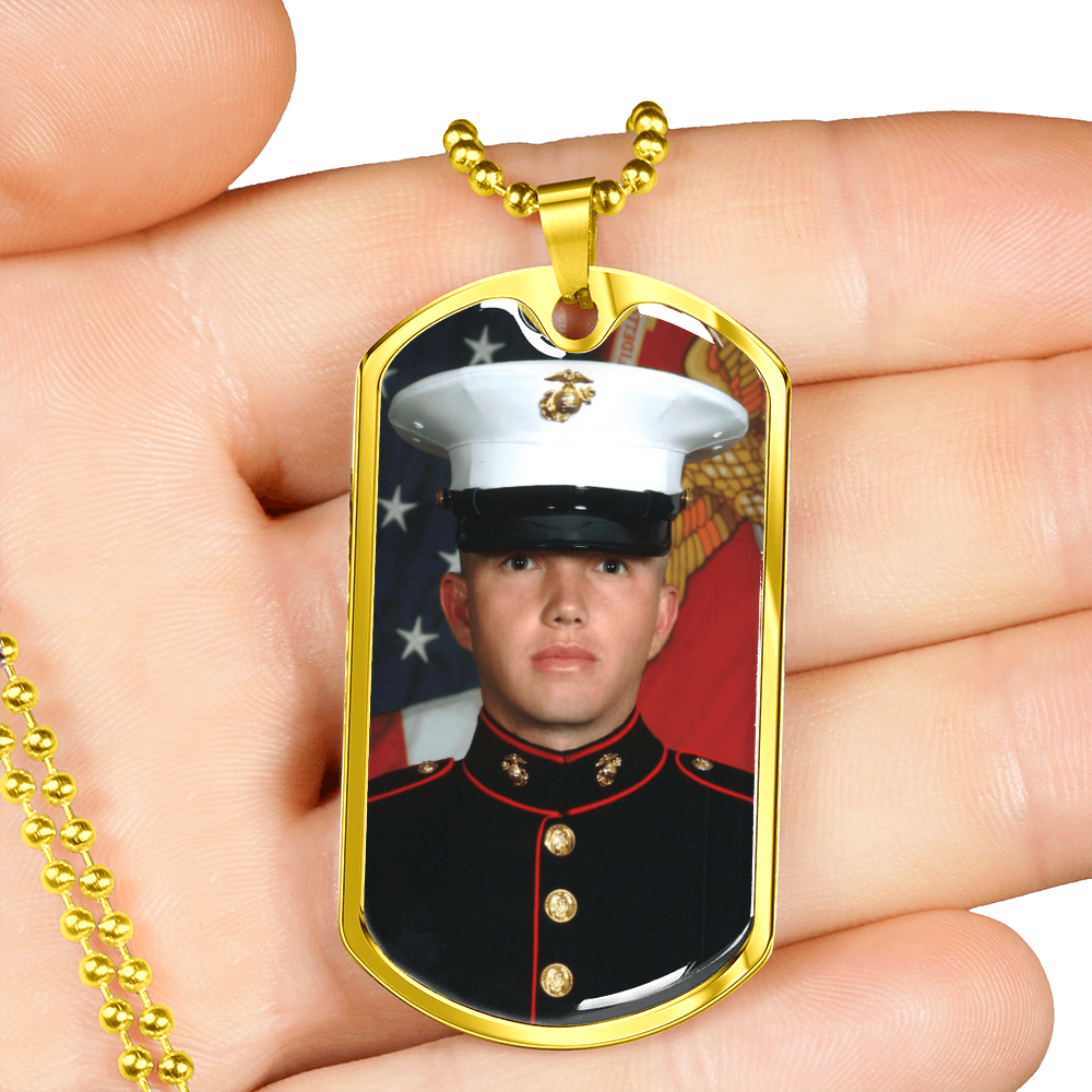 A hand holding a gold custom photo dog tag necklace with a gold ball chain, showing a portrait of a U.S. Marine.