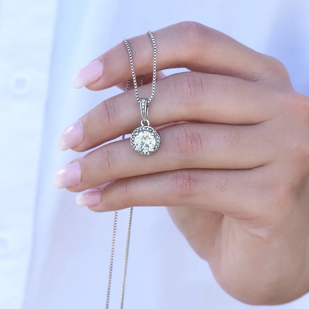 Hand holding a silver necklace with a diamond pendant against a white background