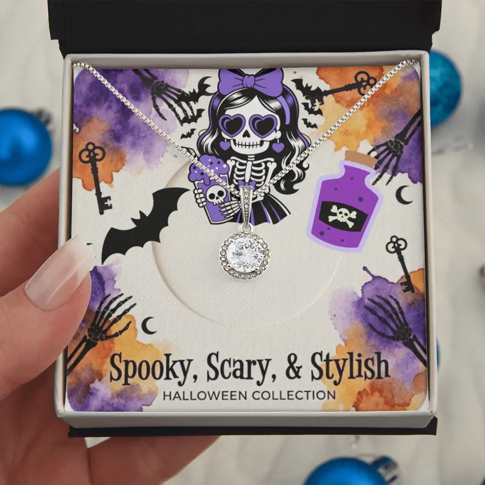 A hand holds an open gift box containing a Halloween-themed necklace. The necklace has a silver-toned skeleton pendant with a purple skull and crossbones charm and a clear rhinestone heart-shaped pendant.