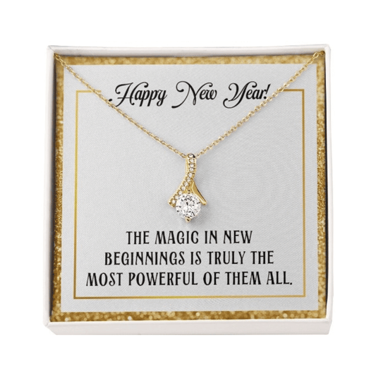 A gold-colored pendant necklace featuring a large, round-cut central crystal dangling from a ribbon-shaped bail encrusted with smaller crystals. The necklace is displayed inside a square white gift box with a sparkling gold glitter border. 
