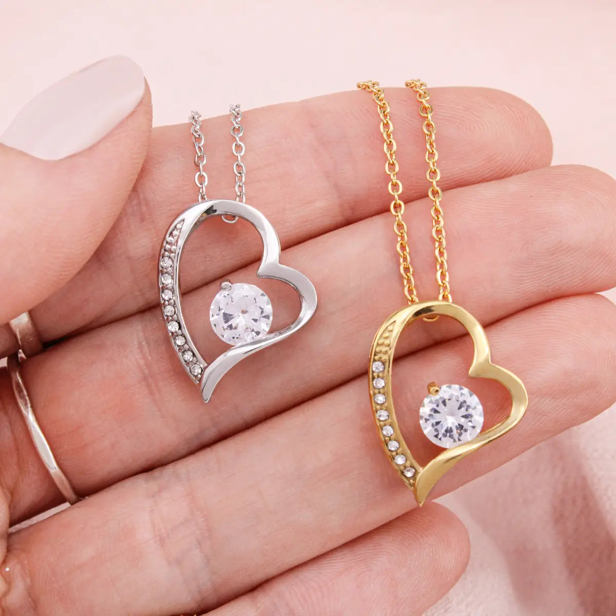 a silver and gold heart pendant and chain displayed on the palm of a hand with a soft pink background.