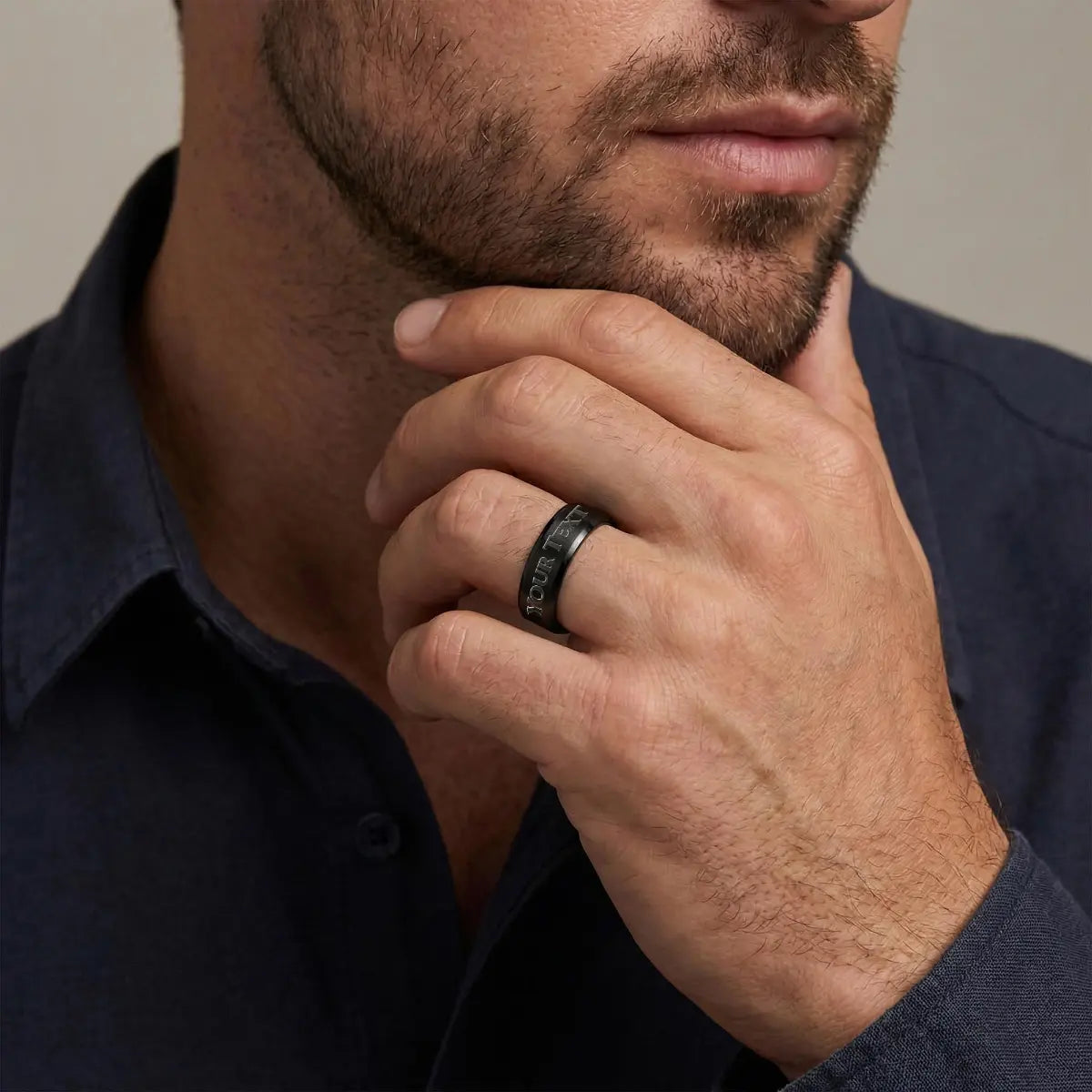 a man with a dark gray shirt and light black beard with a black steel ring on his finder that says YOUR TEXT, with a light gray background.