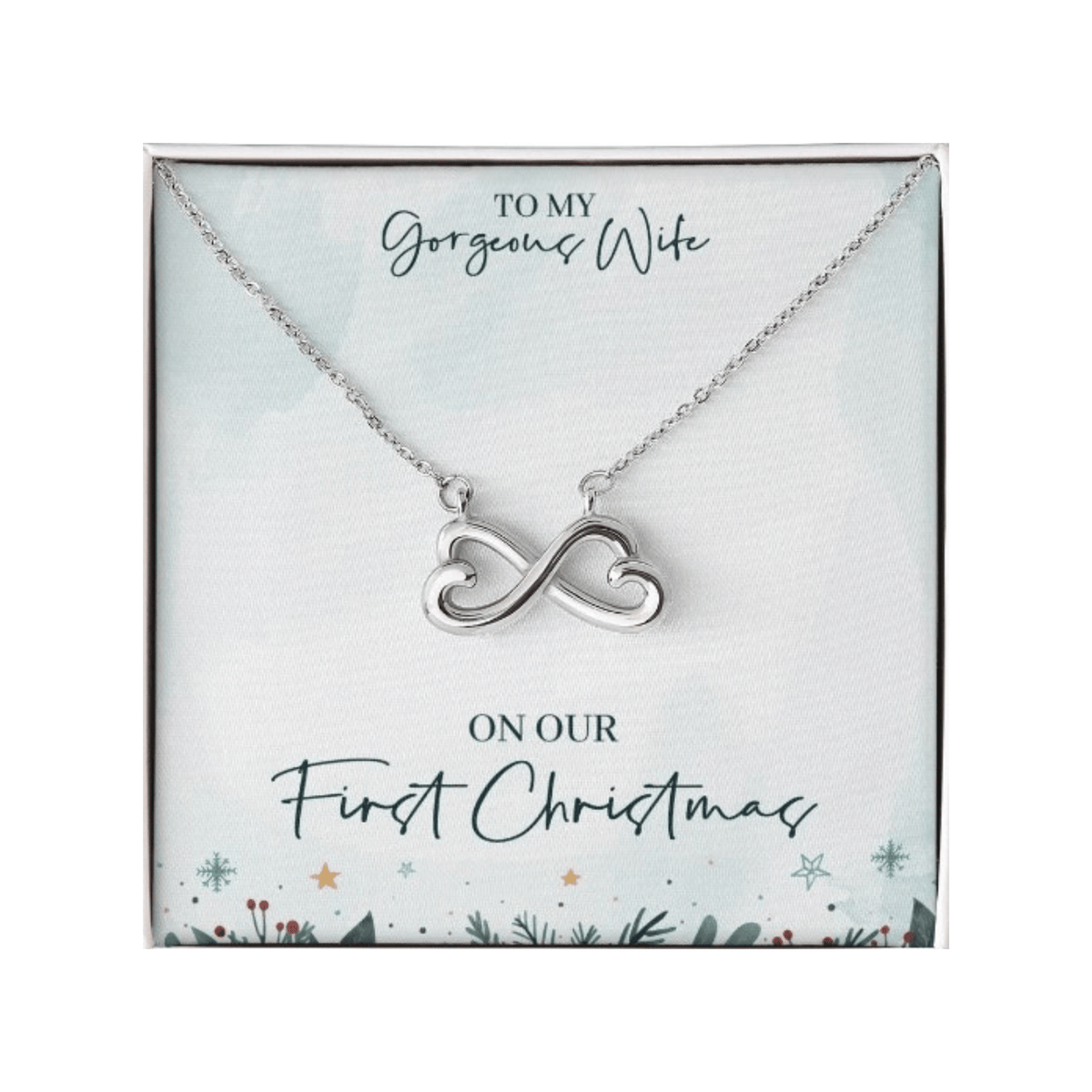 A silver infinity symbol necklace shaped with two hearts inside a gift box. The background card features festive evergreen branch, snowflake, and star illustrations with the text: "TO MY Gorgeous Wife ON OUR First Christmas".