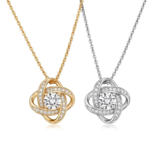 Two love knot pendant necklaces side-by-side on a plain background, one crafted in 18k yellow gold and the other in 14k white gold. Each necklace features an intertwined ribbon design encrusted with small pave crystals surrounding a brilliant round-cut center cubic zirconia stone.