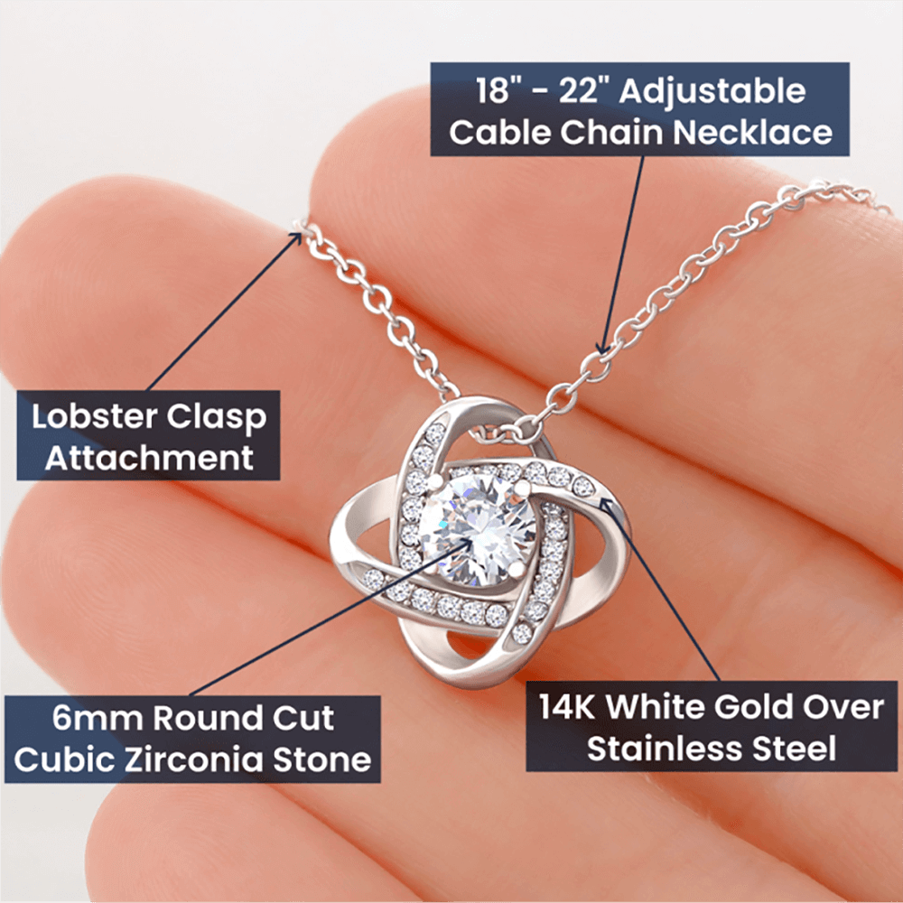 A product infographic image of a silver love knot pendant necklace held in a hand. Text pointers label the jewelry's key features: an 18-to-22-inch adjustable cable chain necklace, a lobster clasp attachment, a 6mm round-cut cubic zirconia stone, and 14k white gold over stainless steel material.