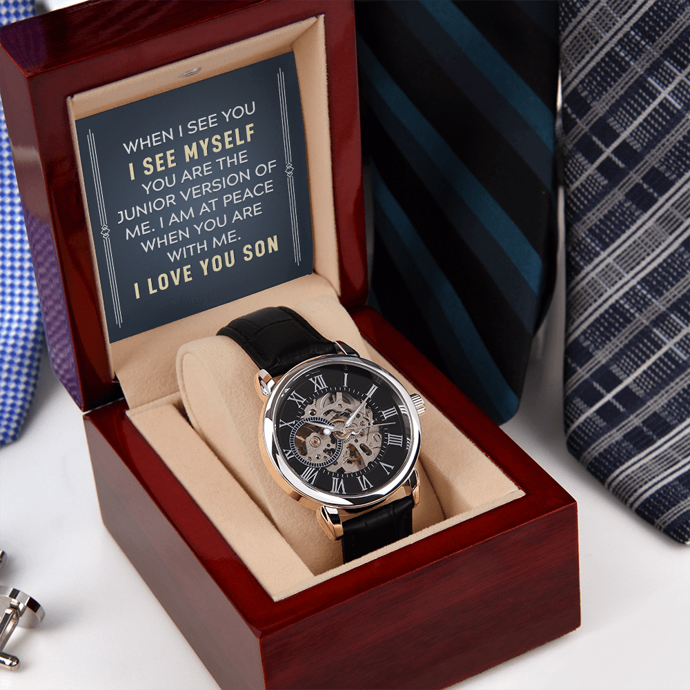 A close-up view of a men's openwork skeleton automatic watch with a black case back, resting inside an open luxury wooden gift box illuminated by an integrated LED light. The background features a neat, organized row of assorted men's ties displayed on a wooden surface.