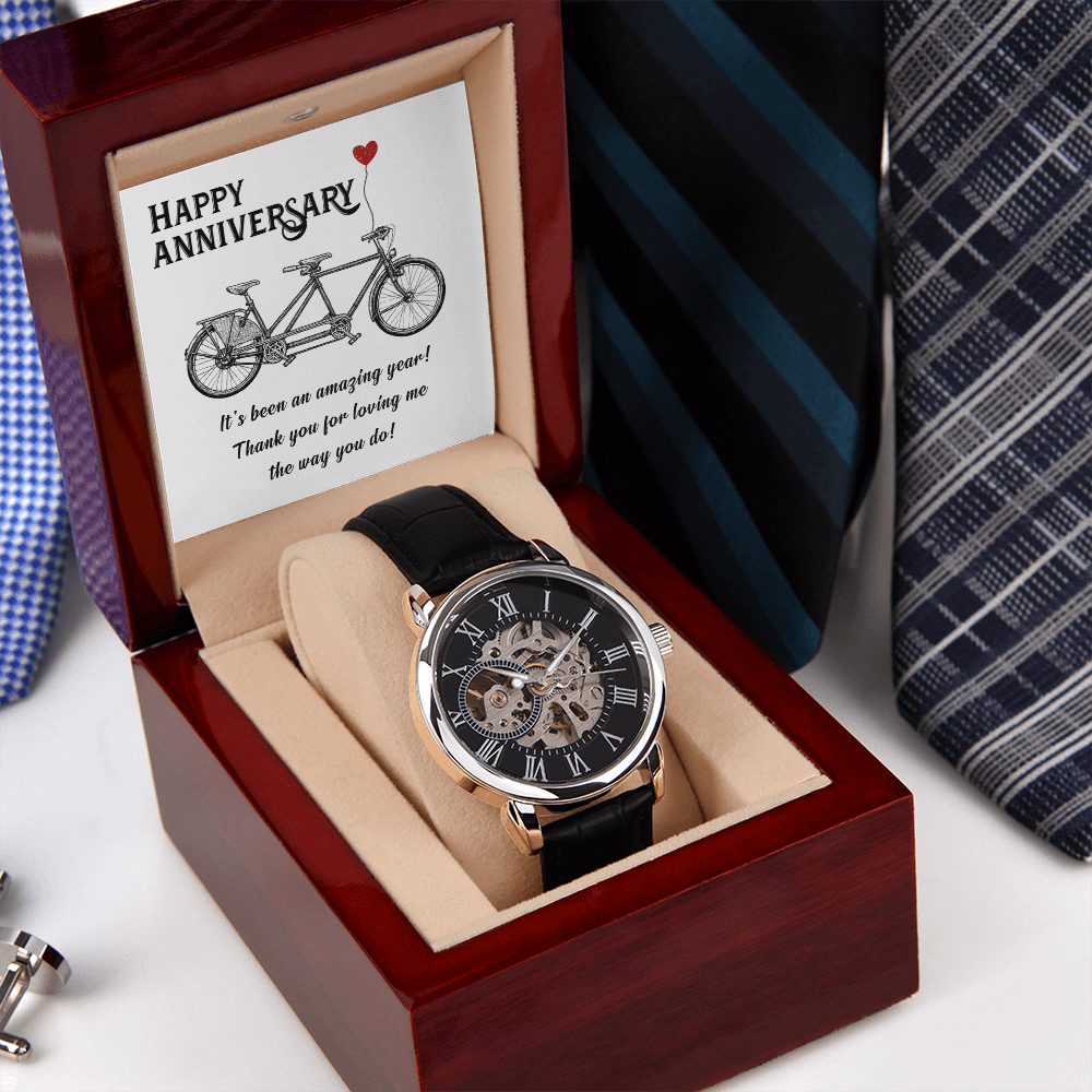 A close-up view of a men's openwork skeleton automatic watch with a black case back, resting inside an open luxury wooden gift box illuminated by an integrated LED light. The background features a neat, organized row of assorted men's ties displayed on a wooden surface.