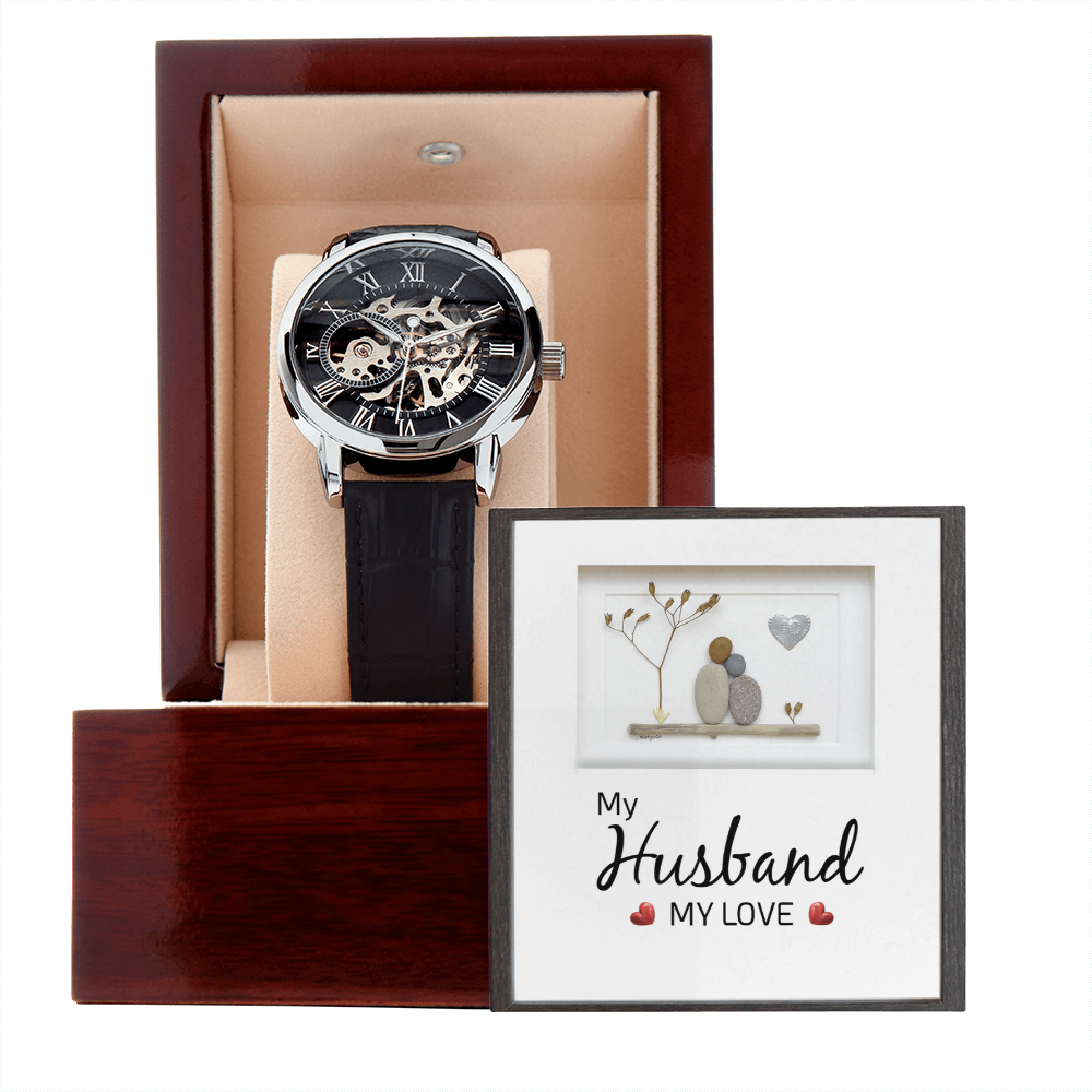 A direct front view of a luxury men's openwork skeleton automatic watch with a black leather strap, presented side-by-side with a personalized romantic sentimental message card for a husband inside an open premium mahogany gift box.