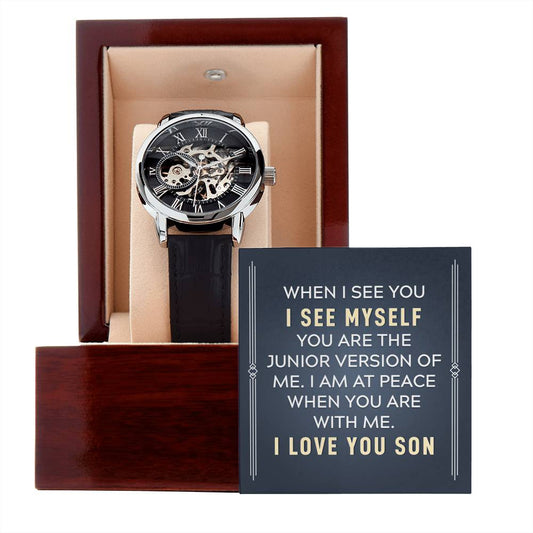 Men's openwork skeleton automatic watch with stainless steel casing and genuine leather band, displayed inside an illuminated luxury mahogany gift box with a soft LED spotlight down onto a personalized sentimental message card for a son.