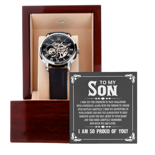 Men's openwork skeleton automatic watch with stainless steel casing and genuine leather band, displayed inside an illuminated luxury mahogany gift box with a soft LED spotlight shining down onto a personalized sentimental message card for a son.