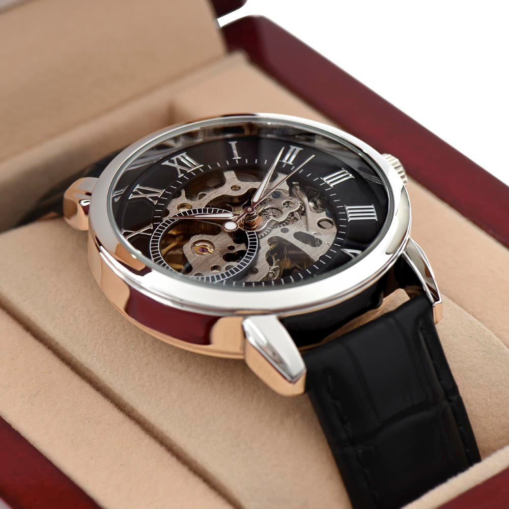 Close-up product photograph of a luxury men's openwork mechanical watch with a genuine leather strap, resting securely inside a plush beige interior lining of an open mahogany wood gift box illuminated by an integrated spotlight.