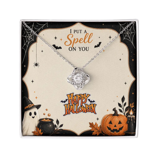 A silver-toned crystal ball necklace displayed on a decorative Halloween-themed gift card. The card features the phrase 'I PUT A Spell ON YOU' at the top and 'Happy Halloween' at the bottom, decorated with spiderwebs, a ghost, a cauldron, and a jack-o'-lantern pumpkin.