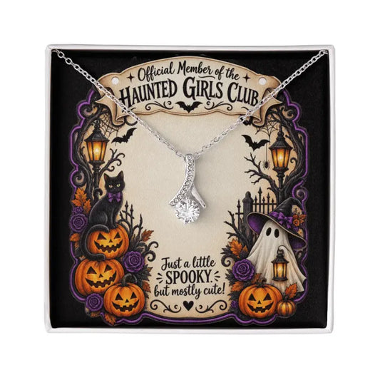 A silver-toned necklace with a clear crystal pendant displayed on a decorative Halloween-themed gift card. The card features the text 'Official Member of the Haunted Girls Club' and 'Just a little spooky but mostly cute!' with illustrations of pumpkins, a ghost, a cat, and lanterns.