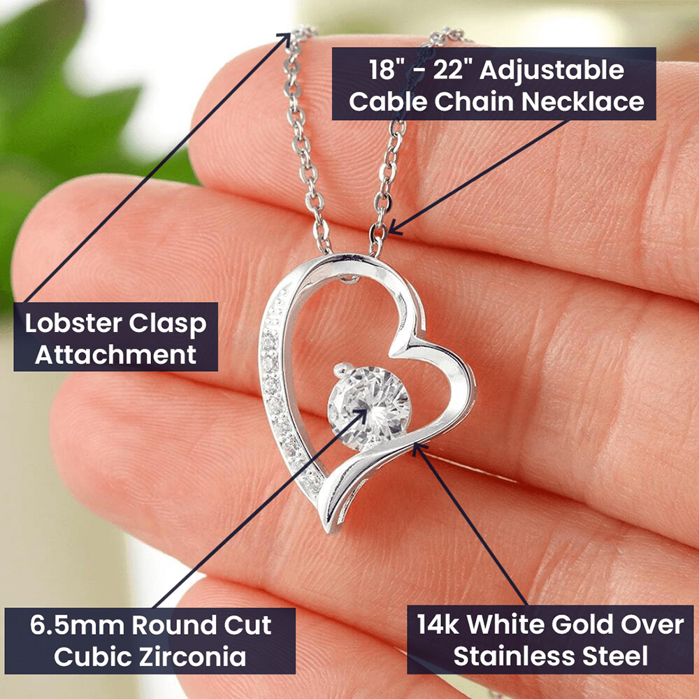 Close-up product photo of a silver-tone heart-shaped pendant necklace held between fingers. The pendant features a sparkling round-cut cubic zirconia centerpiece and a curved heart design accented with smaller stones. Text callouts highlight the 18–22 inch adjustable cable chain, lobster clasp attachment, 6.5mm round-cut cubic zirconia, and 14K white gold over stainless steel.