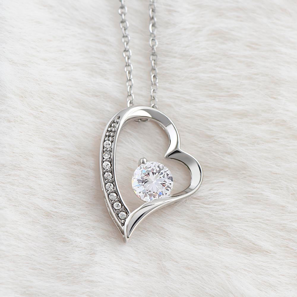Silver heart-shaped pendant necklace with a large round sparkling gemstone and smaller accent stones, displayed on soft white fur.
