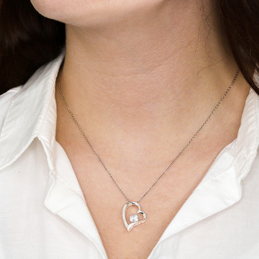 Silver heart pendant necklace with a delicate chain, worn by a woman in a white collared shirt.
