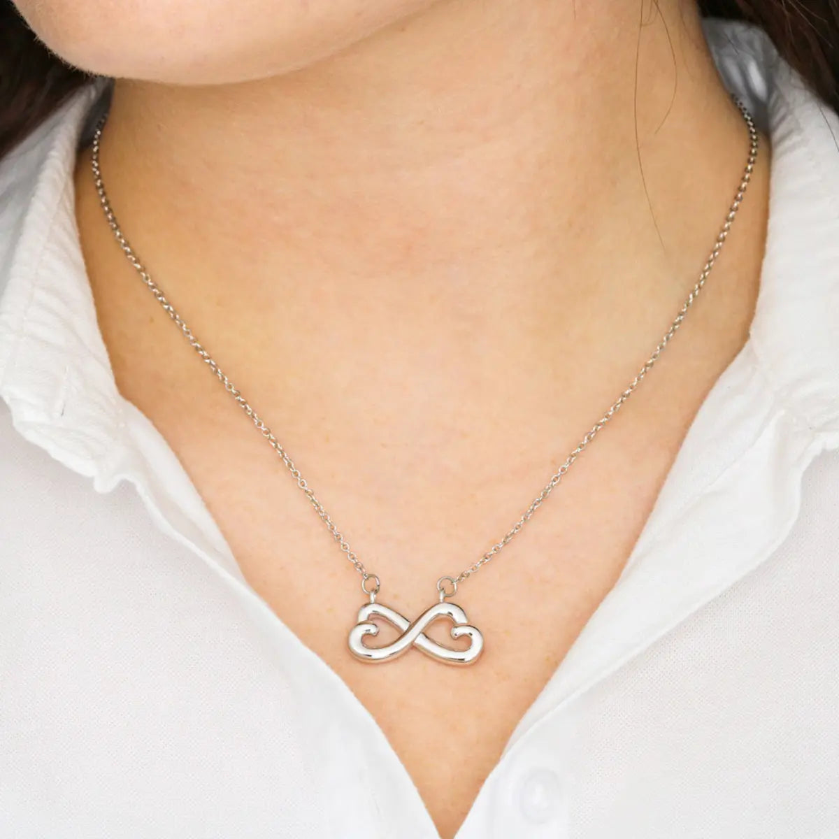 Silver infinity necklace worn by a person on a white shirt background