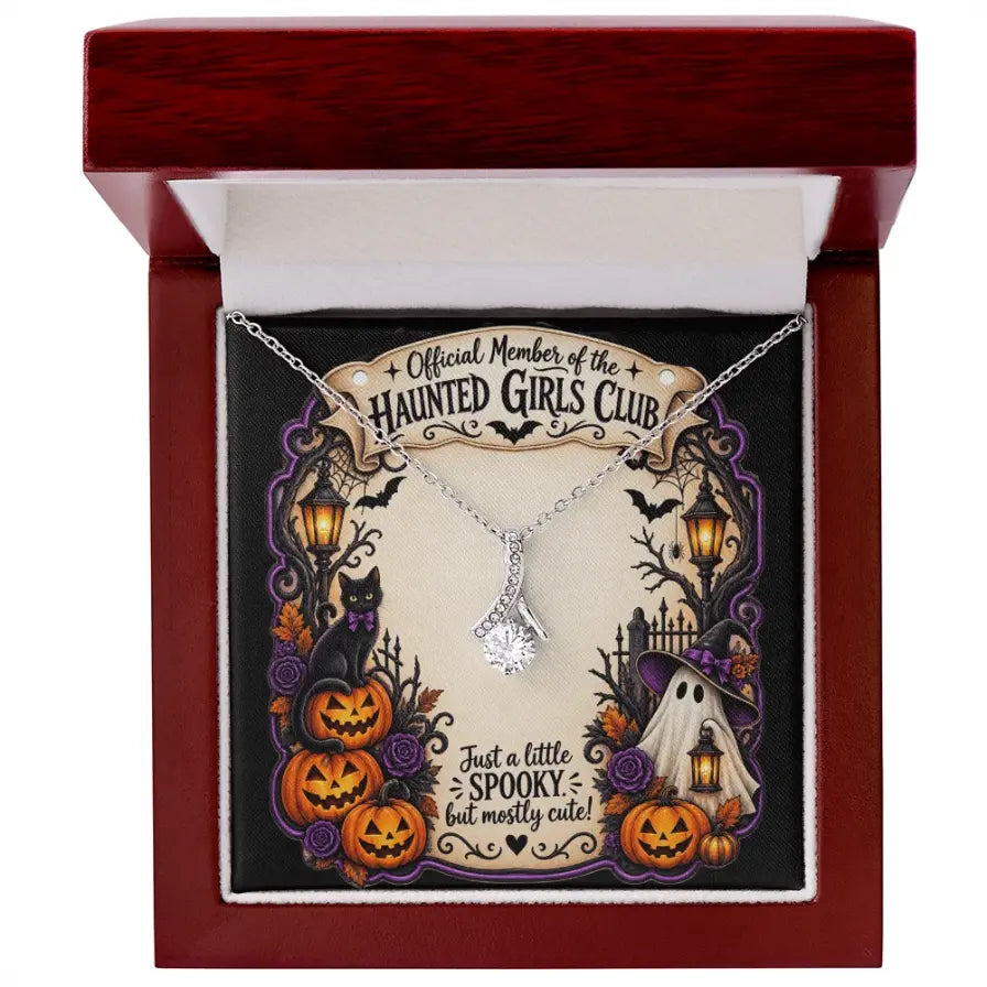 A silver necklace with a clear rhinestone pendant displayed inside an open dark red gift box. The necklace is mounted on a decorative Halloween-themed card that reads 'Official Member of the Haunted Girls Club' and 'Just a little spooky, but mostly cute!'.