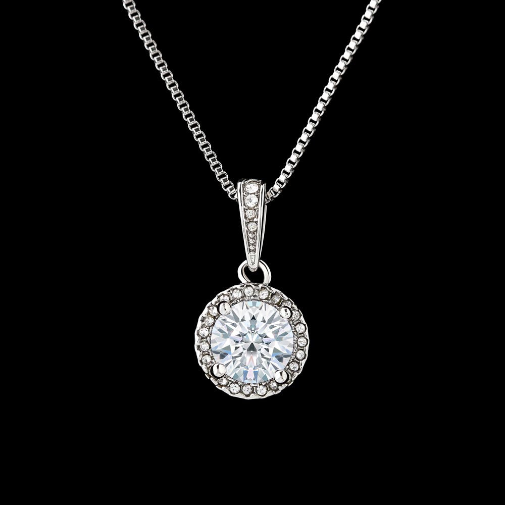A silver round halo pendant necklace featuring a large, brilliant-cut central gemstone encircled by small pavé-set stones, hanging vertically from a classic box chain against a solid black background.