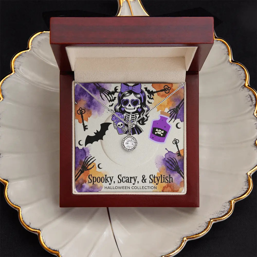 An open dark wood jewelry gift box displayed on a white scalloped plate with gold trim. The box contains a Halloween-themed card and a silver-toned necklace with a skull pendant.