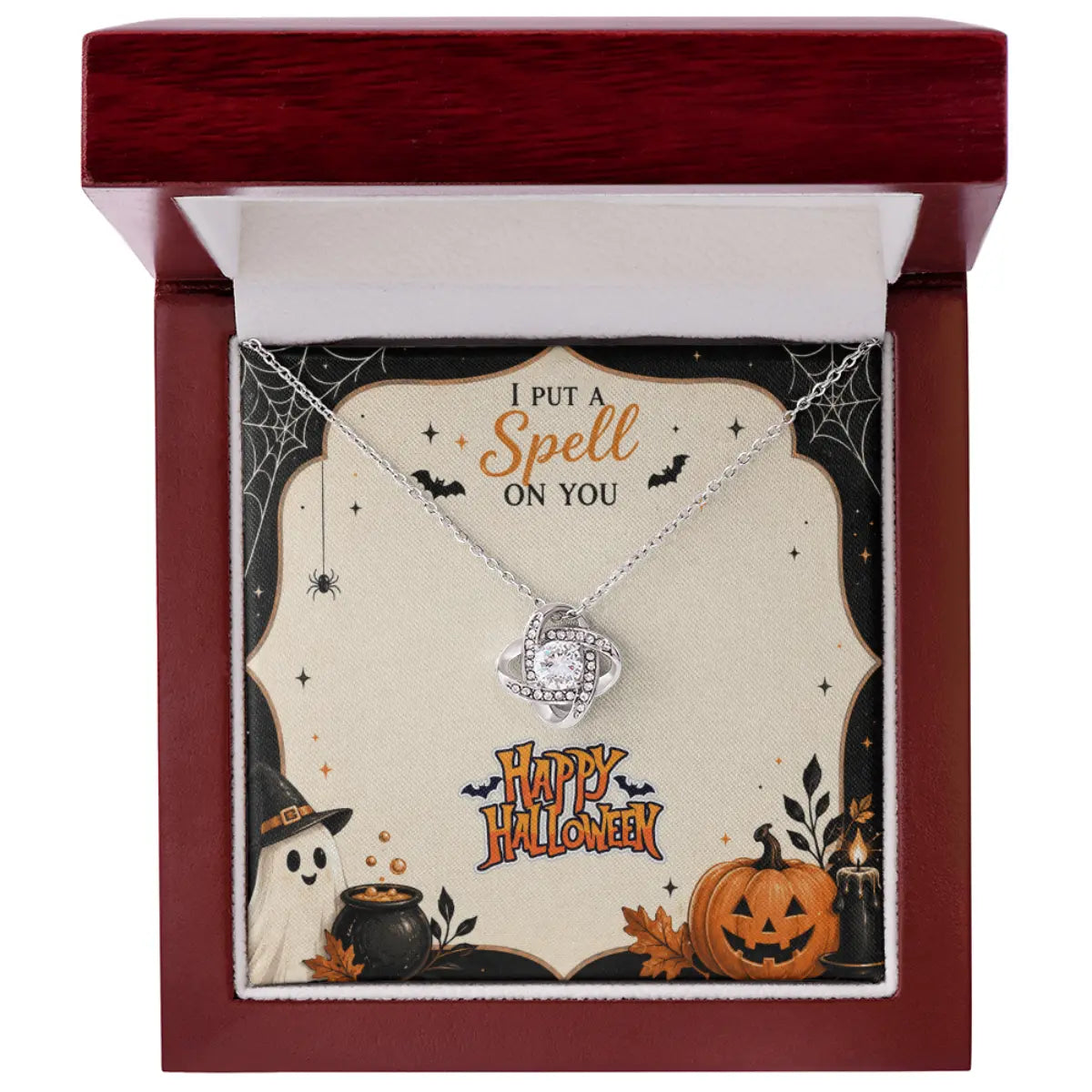 A silver necklace with a swirling crystal pendant is displayed inside an open dark red wooden gift box. The necklace is laid over a decorative Halloween-themed card that reads 'I PUT A Spell ON YOU' and 'Happy Halloween,' with spiderwebs, a witch hat, cauldron, ghost, and jack-o'-lantern illustrations.