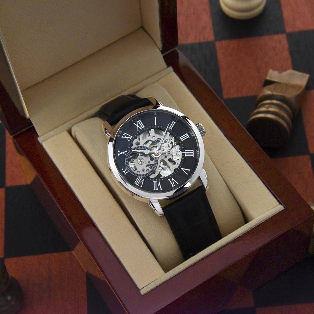 Watch with black strap and skeleton face in an open wooden box on a checkered surface