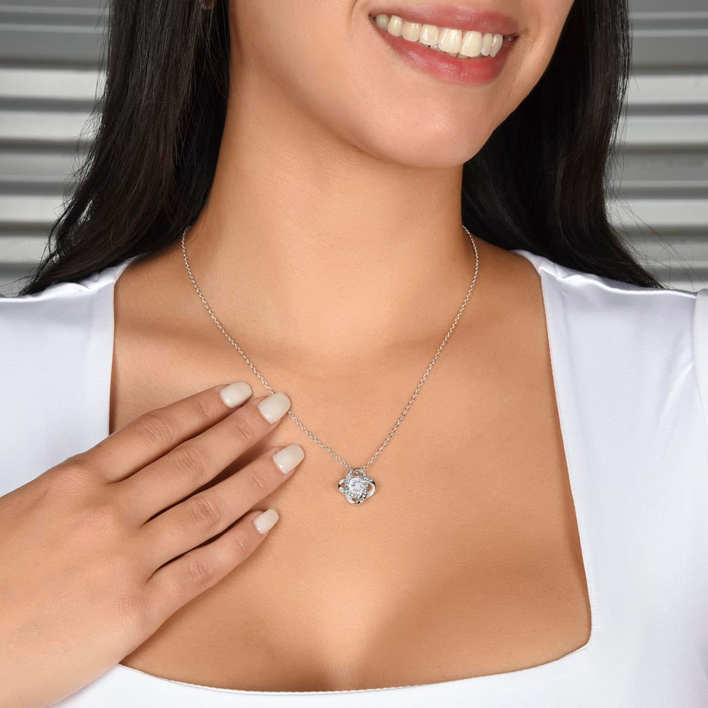 A woman in a white blouse with long dark brown hair wearing a silver chain and knot-shaped pendant with cubic zirconia necklace.